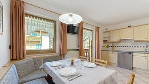 Ruokailutila, jossa on neljälle katettu ruokapöytä, sohva, televisio ja taustalla keittiö.