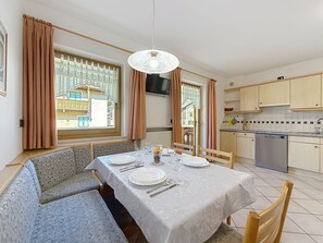 Ein Essbereich mit einem Tisch für vier Personen, einer Couch, einem Fernseher und einer Küche im Hintergrund.