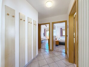 Ein Flur mit Fliesenboden, Holztüren und einem Bett, das durch eine offene Tür zu sehen ist.