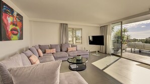 Een moderne woonkamer met een hoekbank, een flatscreen-televisie en een balkon met uitzicht.