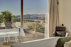 Ein Balkon mit Blick auf eine Stadtlandschaft und ein Gewässer, eine Sitzecke mit Sofa und Kissen sowie ein Blumentopf.