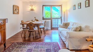 A cozy room with a dining table, chairs, a sofa, a radiator, and a window with a view of greenery. - Campicioi by Interhome (Pinzolo)