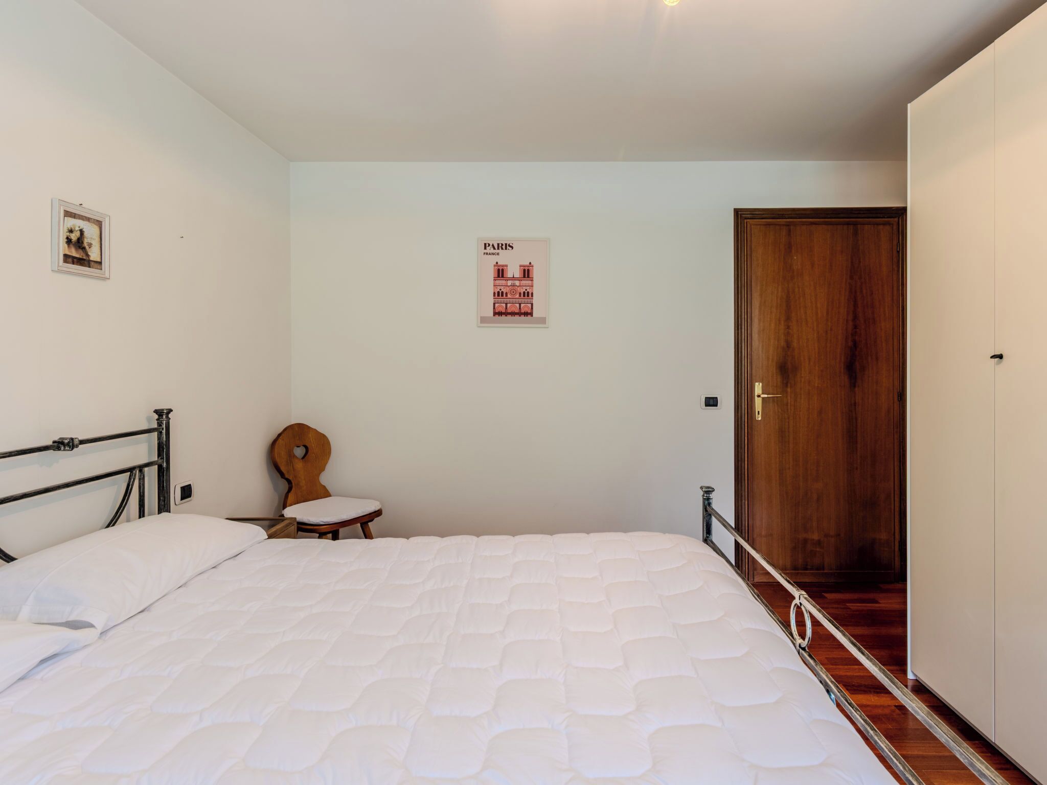 A bedroom with a bed, a wooden chair, a door, and a poster on the wall.