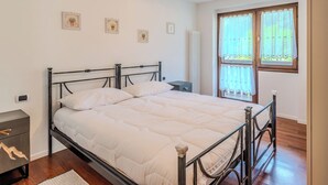 A bedroom with a bed, a bedside table, a nightstand, a window with curtains, and wall-mounted pictures. - Campicioi by Interhome (Pinzolo)