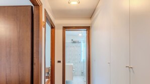 A hallway with wooden flooring, a white door, and a view into a bathroom with a shower and toilet. - Campicioi by Interhome (Pinzolo)