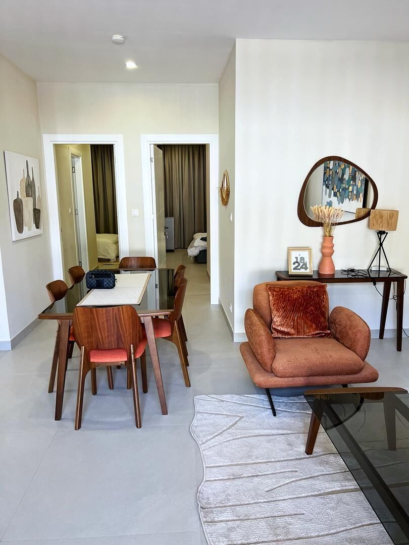A dining area with a glass table and wooden chairs, a sofa with a cushion, and a decorative mirror.