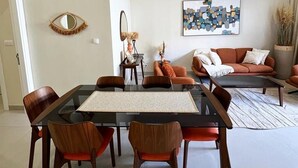 A modern living room with a glass dining table, wooden chairs, a sofa, and a wall-mounted mirror. - CMH SARL (Mbour)