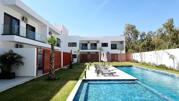 A modern building with a swimming pool, a covered patio, and a well-maintained lawn. - CMH SARL (Mbour)