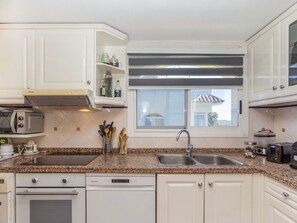 A kitchen with white cabinets, a granite countertop, a built-in dishwasher, a double sink, and a window above the sink.