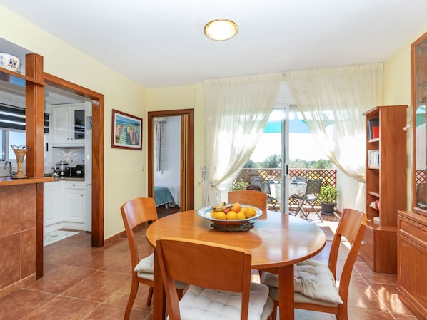 A dining area with a round table, chairs, a bowl of fruit, and a view of the outdoors.