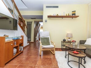 A living room with a sofa, a chair, a coffee table, a TV, a bookshelf, and a staircase.