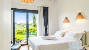 Een slaapkamer met een bed, uitzicht op groen en gebouwen, en twee wandlampen.