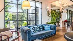 Een ruime woonkamer met een blauwe bank, grote ramen en een kroonluchter.