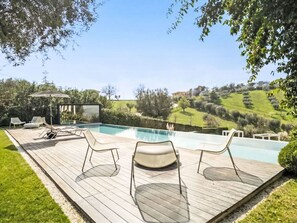 A pool area with lounge chairs, a glass enclosure, and a view of a hilly landscape. - Idea 18 by Interhome (Controguerra)