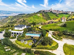 A modern house with a swimming pool, surrounded by well-maintained gardens and a view of a distant town. - Idea 18 by Interhome (Controguerra)