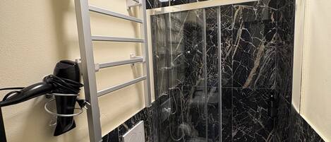 Un baño moderno con ducha envuelta en vidrio, un perchero y un secador de pelo.