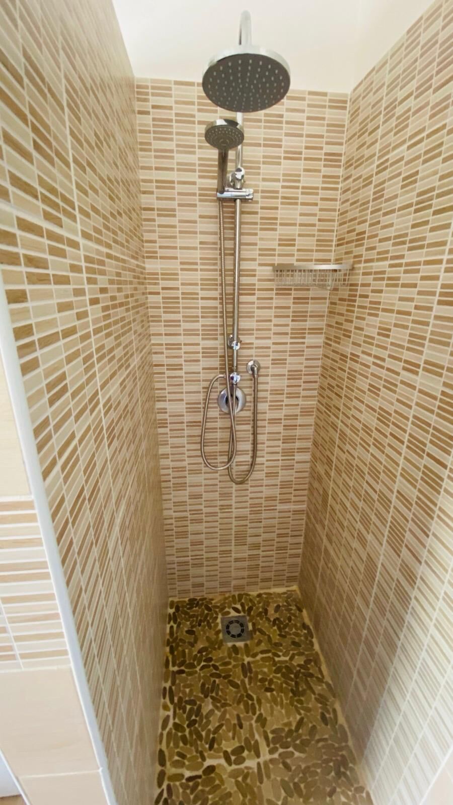 A shower with a rain showerhead, handheld showerhead, and a wall-mounted control.