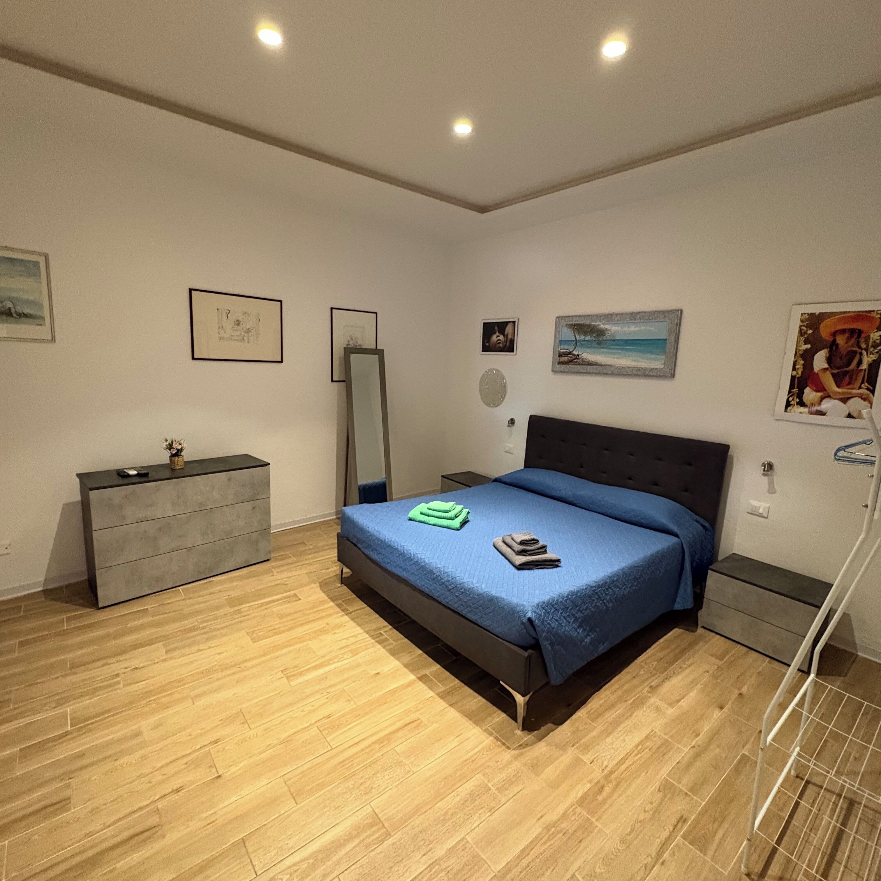 Un dormitorio con cama, mesitas de noche, cómoda y obras de arte en las paredes.