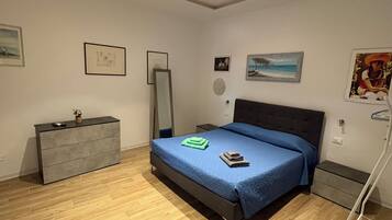 Un dormitorio con cama, mesitas de noche, cómoda y obras de arte en las paredes.