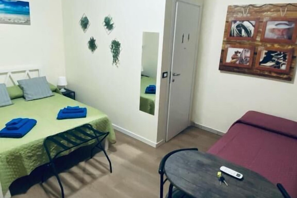 A room with a bed, a small table, a mirror, and a door.