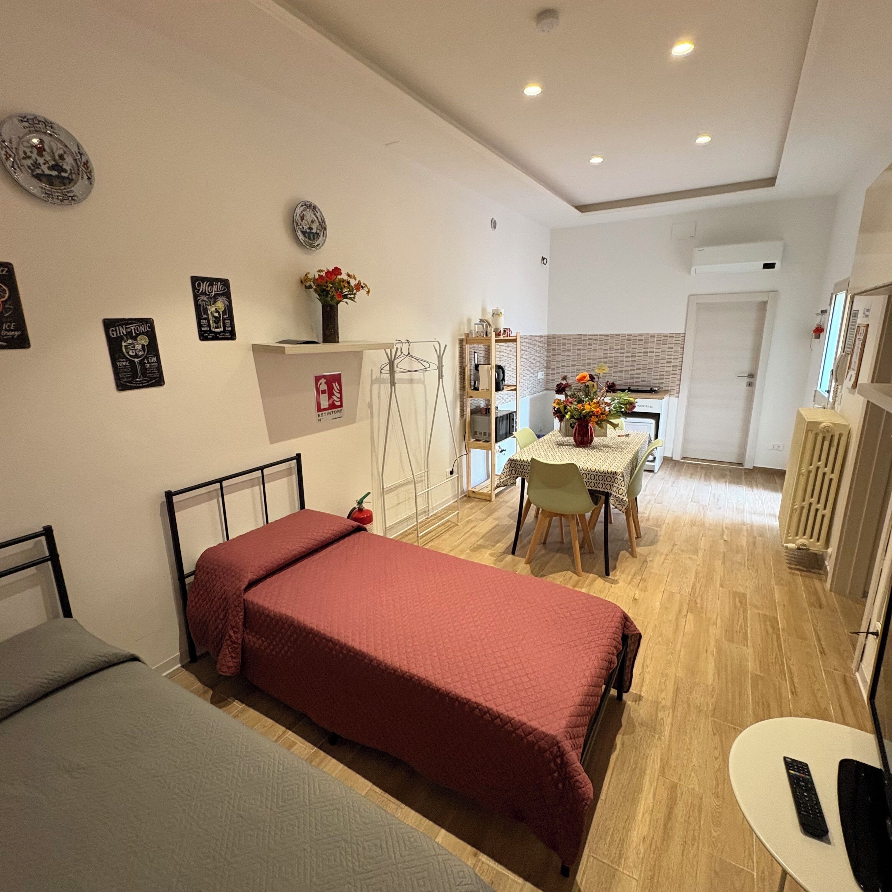A compact room with a bed, a small table, and a kitchenette area.