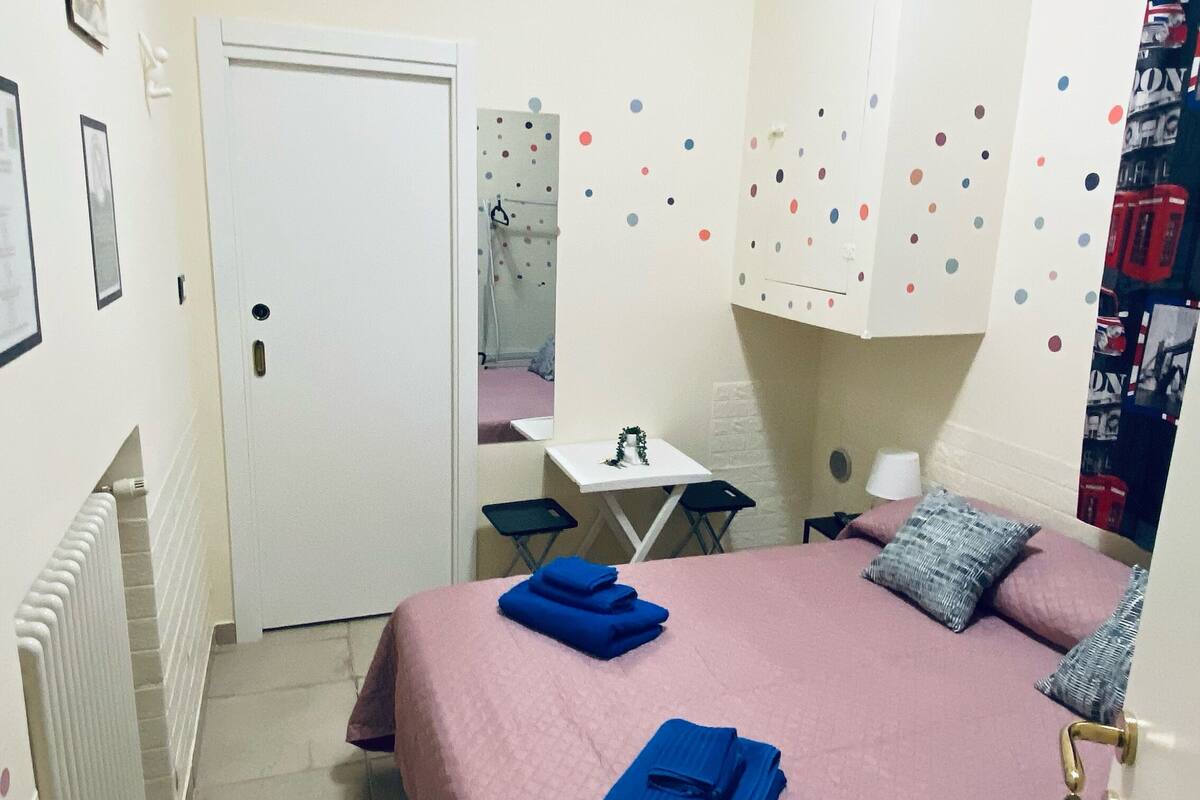 Ein Schlafzimmer mit Bett, Schreibtisch, Stuhl, Heizkörper und einer Tür.