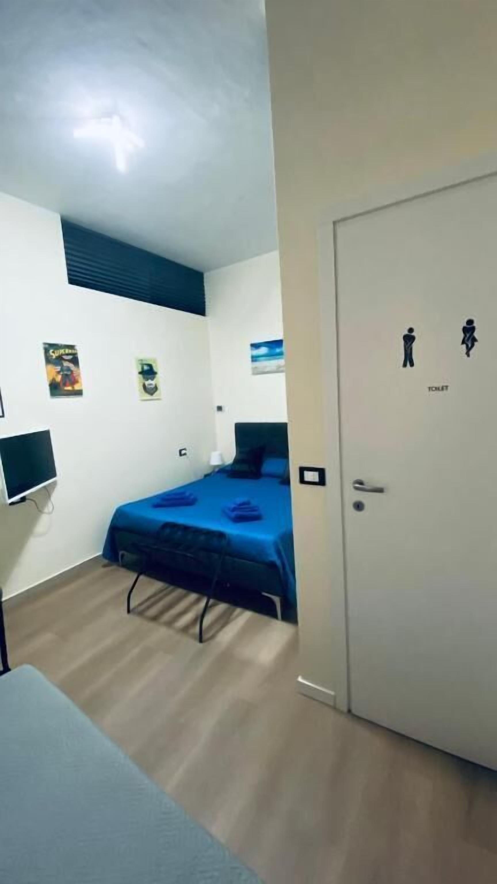 A bedroom with a bed, a desk, and a door with a toilet symbol.