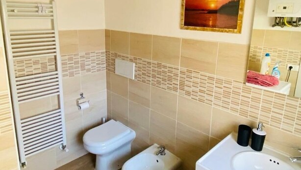 A bathroom with a toilet, bidet, and sink, tiled walls, and a wooden floor.