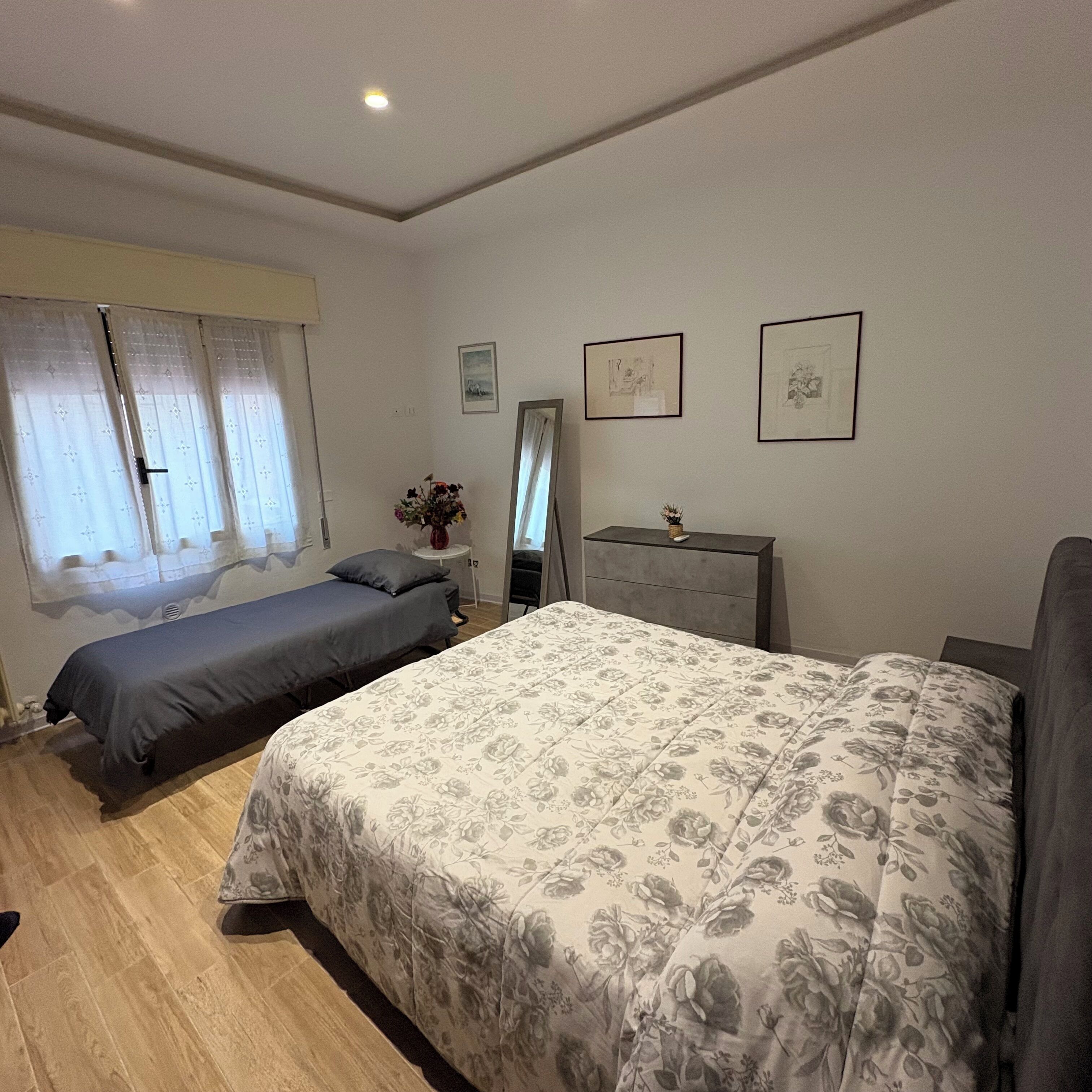 A bedroom with a large bed, a smaller bed, a dresser, and a mirror.