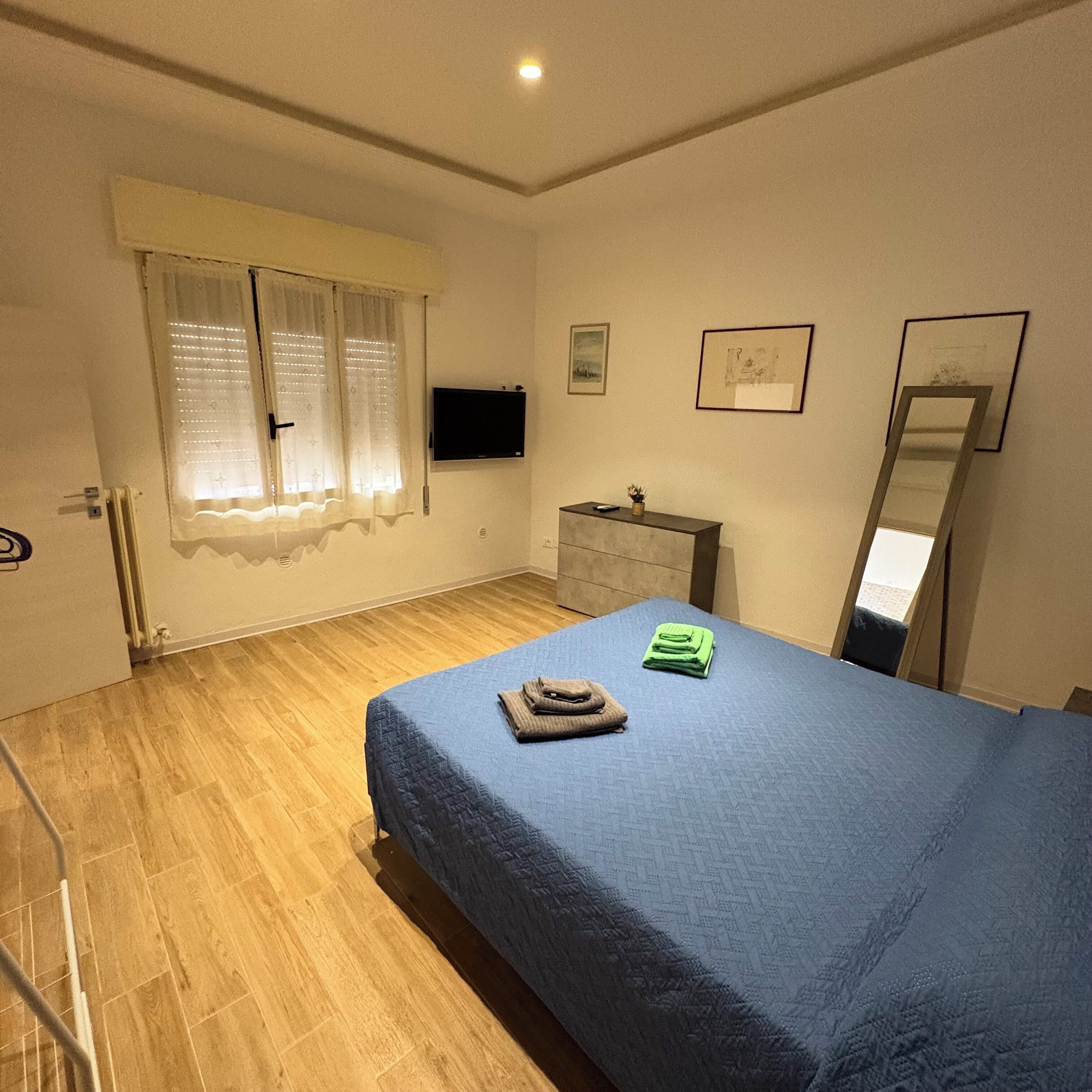 Een slaapkamer met een bed, een dressoir, een televisie en een raam met gordijnen.