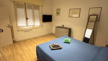 Een slaapkamer met een bed, een dressoir, een televisie en een raam met gordijnen.
