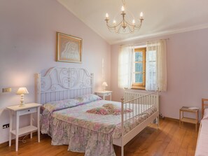 A bedroom with a bed, bedside tables, a chandelier, a window with curtains, and a framed picture on the wall. - Casa dei Nonni by Interhome (Stazzema)