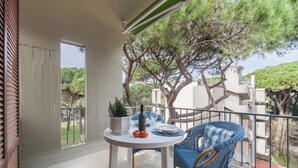Un balcone con tavolo e sedie, una pianta in vaso e vista su alberi ed edifici.