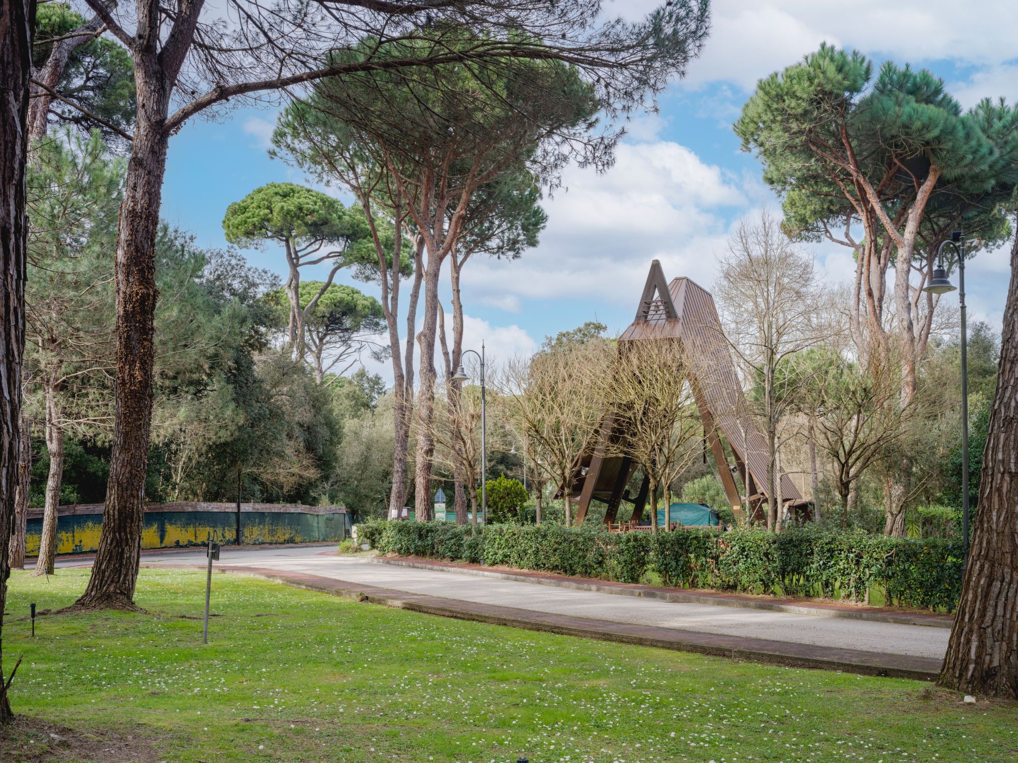 Um parque com árvores, um caminho sinuoso e uma escultura metálica singular.