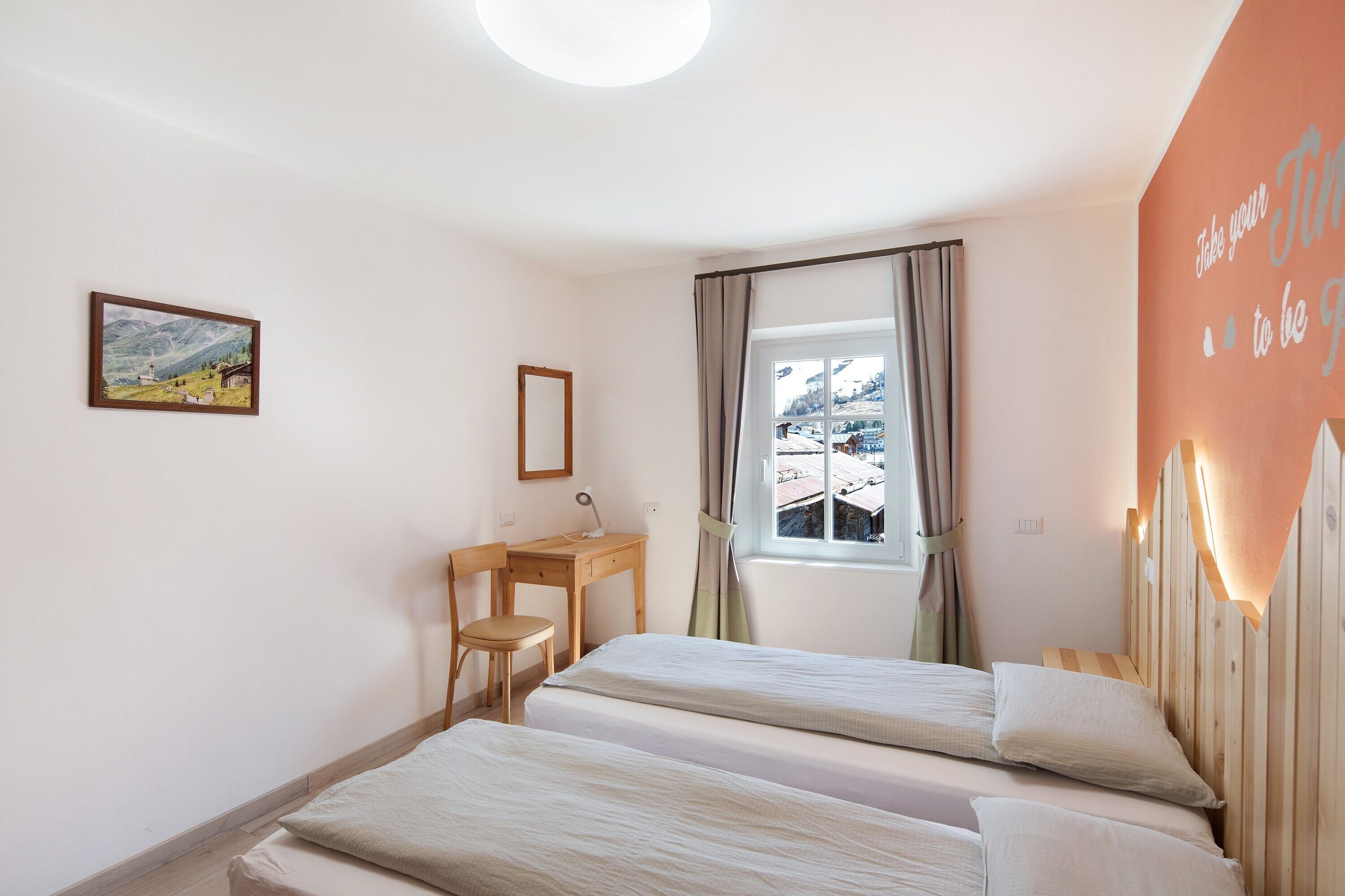 Ein Schlafzimmer mit zwei Betten, einem Schreibtisch, einem Stuhl, einem Fenster mit Vorhängen und einem Wandbild.