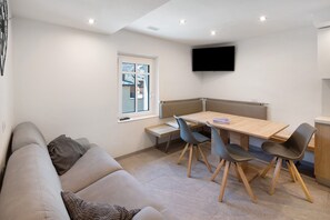 Ein modernes Wohnzimmer mit einer Couch, einem Esstisch mit Stühlen, einem an der Wand montierten Fernseher und einem Fenster mit Blick.