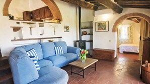 Ein Wohnzimmer mit einem blauen Sofa, einem Holztisch und einem durch einen Durchgang sichtbaren Küchenbereich.