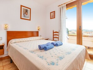 A bedroom with a bed, two wall-mounted lamps, a wooden chair, a window with a view, and a door. - Raco Mas Estel by Interhome (L'Escala)