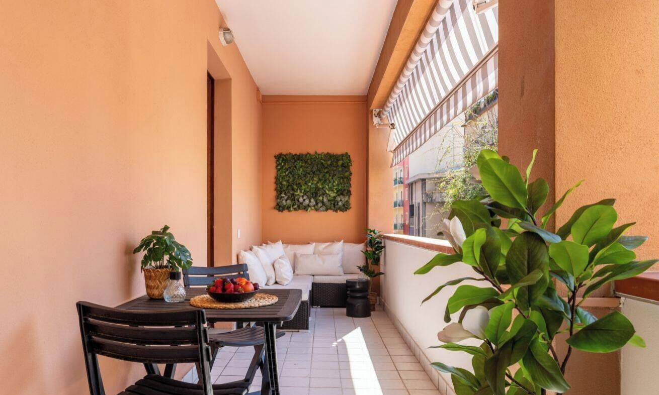 Un balcón con una mesa, sillas, un sofá y plantas en macetas.