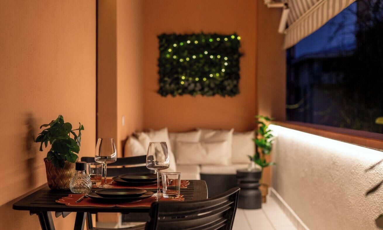 A dining area with a table set for two, a potted plant, and a decorative wall hanging.