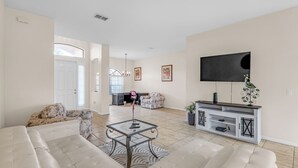 A living room with a sofa, a coffee table, a TV, and a decorative plant. - Retreat Charmz (Kissimmee)