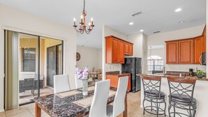 A modern kitchen with wooden cabinets, a marble countertop, and a dining area with a table and chairs. - Retreat Charmz (Kissimmee)