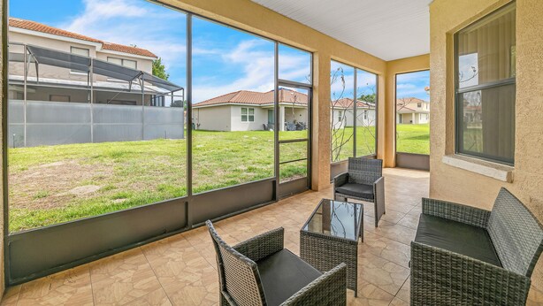 A covered patio area with large windows, wicker furniture, and a view of neighboring houses. - Retreat Charmz (Kissimmee)