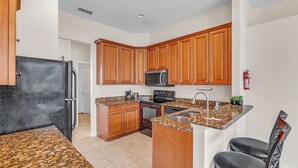 A kitchen with wooden cabinets, a granite countertop, a refrigerator, an oven, a microwave, and a sink. - Retreat Charmz (Kissimmee)
