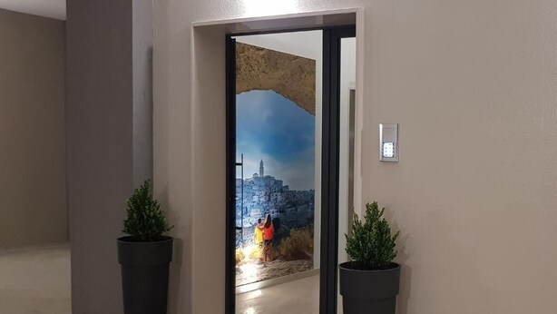 Una puerta que da a una habitación con un mural de la ciudad, dos plantas en macetas y un felpudo negro.