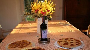 Een tafel met vier taarten, een fles wijn en een vaas vol bloemen.