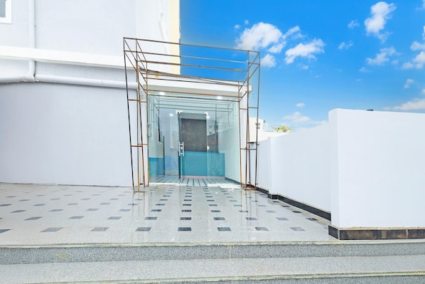A glass-enclosed entrance with a metal frame, a tiled floor, and a clear sky.