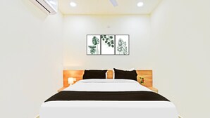 Un lit bien fait, recouvert d’une couvre-lit noire et blanche, avec une tête de lit en bois et une œuvre d’art représentant des feuilles accrochée au mur.