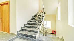 Un escalier avec des marches en marbre et des rampes en métal, une porte en bois et une fenêtre avec des stores.