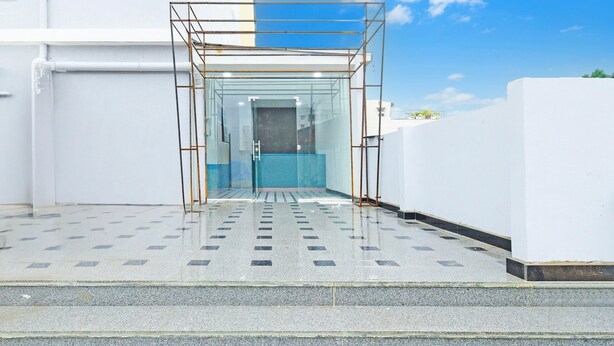 Une entrée moderne, avec une structure en verre, des marches menant à l’intérieur et un ciel dégagé.
